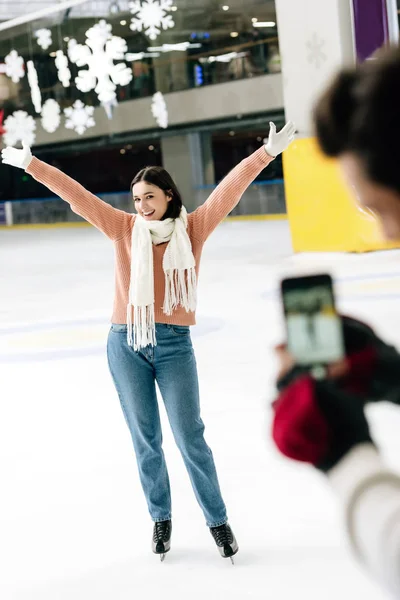 Selective focus of man taking photo of excited woman on smartphone on skating rink — Stock Photo