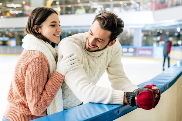 Alegre joven pareja en suéteres pasar tiempo en pista de patinaje - foto de stock