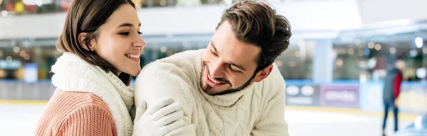 Plan panoramique de jeune couple souriant en chandails passant du temps sur la patinoire — Photo de stock