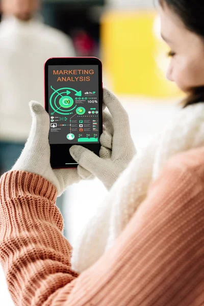 Vista recortada de la mujer en guantes con teléfono inteligente con aplicación de análisis de marketing en la pantalla - foto de stock