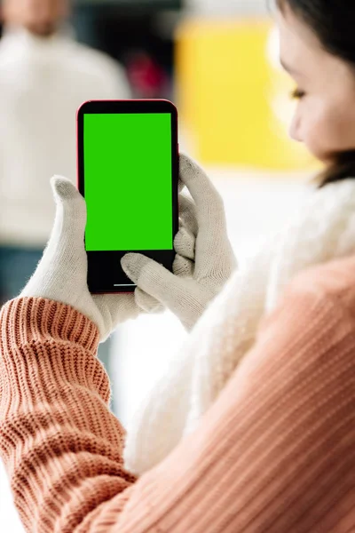KYIV, UCRANIA - 15 DE NOVIEMBRE DE 2019: vista recortada de la mujer en guantes que sostiene el teléfono inteligente con pantalla verde - foto de stock