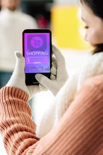 KYIV, UCRAINA - 15 NOVEMBRE 2019: vista ritagliata della donna in guanti che tiene smartphone con app per lo shopping sullo schermo — Foto stock