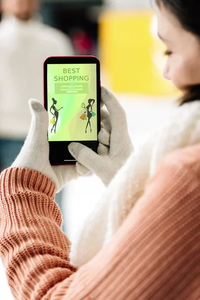 KYIV, UKRAINE - 15 NOVEMBRE 2019 : vue recadrée de la femme en gants tenant un smartphone avec la meilleure application shopping à l'écran — Photo de stock