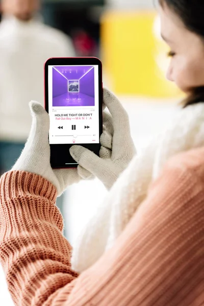 KYIV, UCRAINA - 15 NOVEMBRE 2019: vista ritagliata della donna in guanti che tiene smartphone con app musicale sullo schermo — Foto stock