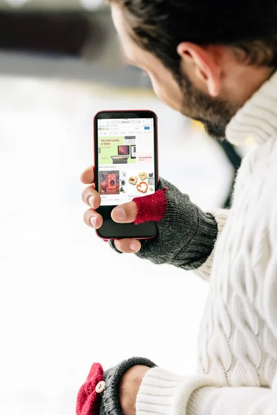KYIV, UKRAINE - NOVEMBRO 15, 2019: visão recortada do homem de luvas segurando smartphone com aplicativo ebay na tela, na pista de patinação — Fotografia de Stock