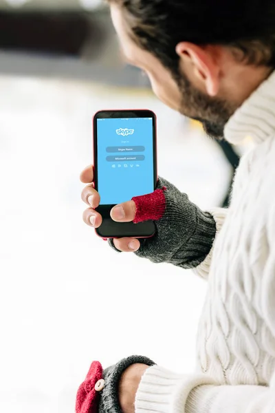 KYIV, UCRANIA - 15 DE NOVIEMBRE DE 2019: vista recortada del hombre con guantes que sostiene el teléfono inteligente con la aplicación skype en la pantalla, en la pista de patinaje - foto de stock