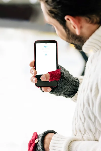 KYIV, UCRANIA - 15 DE NOVIEMBRE DE 2019: vista recortada del hombre con guantes que sostiene el teléfono inteligente con la aplicación skype en la pantalla, en la pista de patinaje - foto de stock
