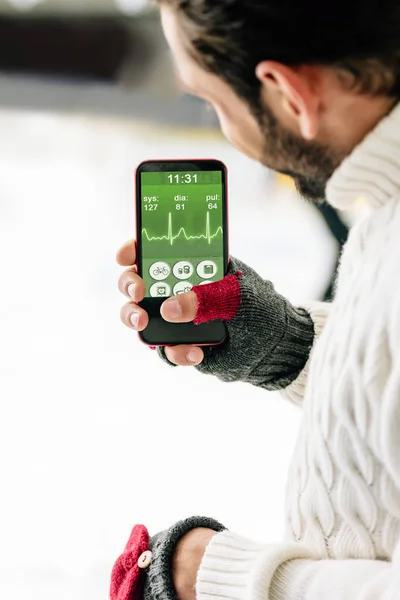 KYIV, UKRAINE - 15 NOVEMBRE 2019 : vue recadrée de l'homme en gants tenant un smartphone avec une application de santé à l'écran, sur une patinoire — Photo de stock