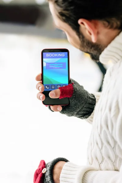 KYIV, UKRAINE - NOVEMBRO 15, 2019: visão recortada do homem de luvas segurando smartphone com aplicativo de reserva na tela, na pista de patinação — Fotografia de Stock