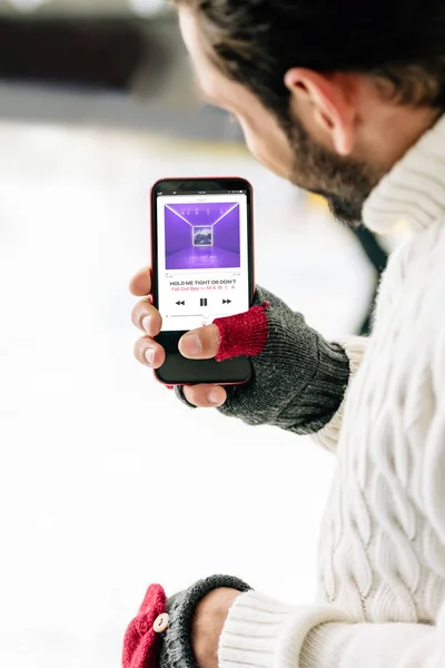 KYIV, UKRAINE - NOVEMBRO 15, 2019: visão recortada do homem de luvas segurando smartphone com aplicativo de música de maçã na tela, na pista de patinação — Fotografia de Stock