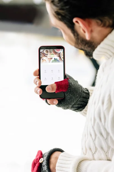 KYIV, UCRANIA - 15 DE NOVIEMBRE DE 2019: vista recortada del hombre en guantes que sostiene el teléfono inteligente con la aplicación foursquare en la pantalla, en la pista de patinaje - foto de stock