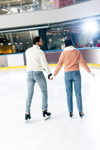 Rückansicht eines jungen Paares beim Händchenhalten und Schlittschuhlaufen auf der Eisbahn — Stockfoto
