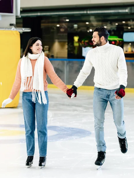 Beautiful happy couple holding hands and spending time on skating rink — Stock Photo
