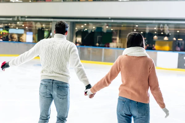 Vista posteriore della giovane coppia che si tiene per mano sulla pista di pattinaggio — Foto stock