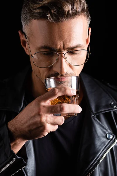Hombre guapo en gafas de sol bebiendo whisky aislado en negro - foto de stock