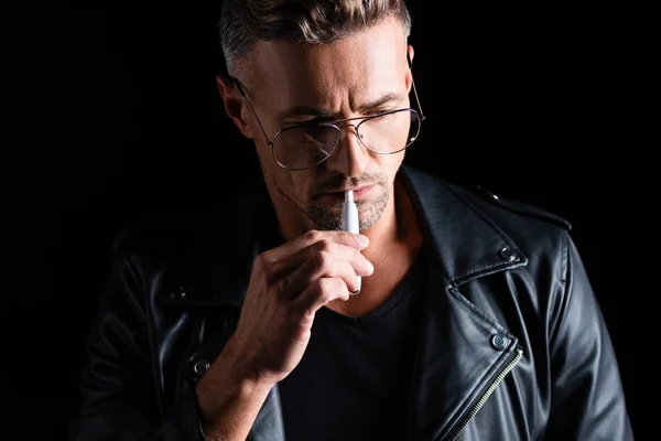 KYIV, UKRAINE - OCTOBER 11, 2019: Handsome pensive man smoking iqos isolated on black — Stock Photo
