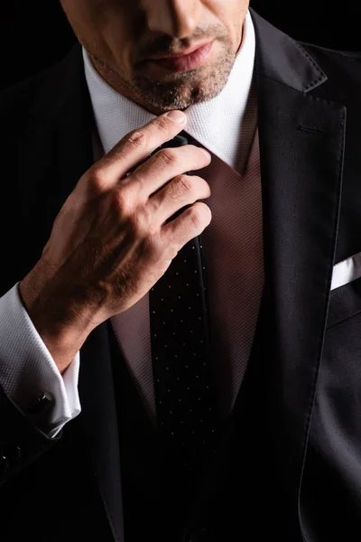 Cropped view of businessman in formal wear regulating tie isolated on black — Stock Photo