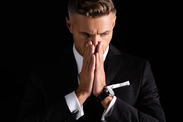 Hombre de negocios pensativo con las manos a la cara mirando hacia otro lado aislado en negro - foto de stock