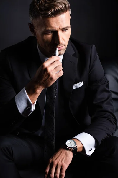 KYIV, UCRANIA - 11 de octubre de 2019: Empresario pensativo fumando iqos aislado en negro — Stock Photo