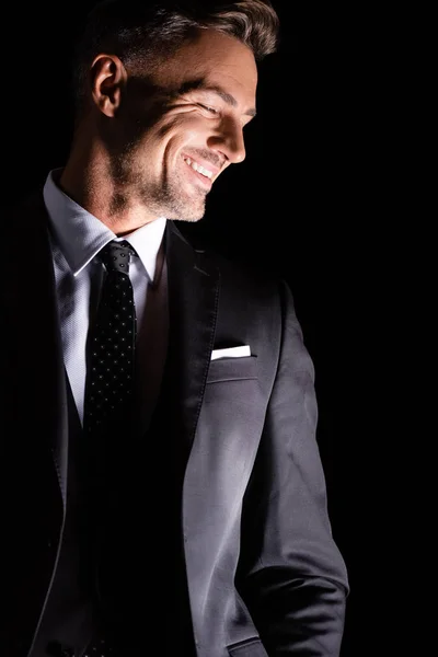 Empresario en ropa formal mirando hacia abajo y sonriendo aislado en negro - foto de stock