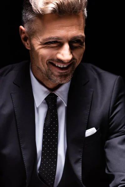 Hombre de negocios sonriente en traje mirando hacia otro lado aislado en negro — Stock Photo