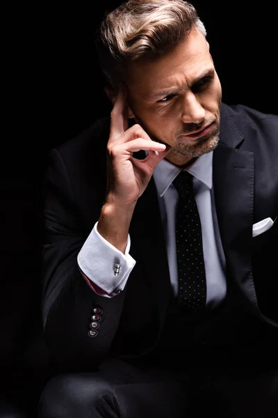 Pensativo hombre de negocios con la mano a la cara mirando hacia otro lado aislado en negro - foto de stock