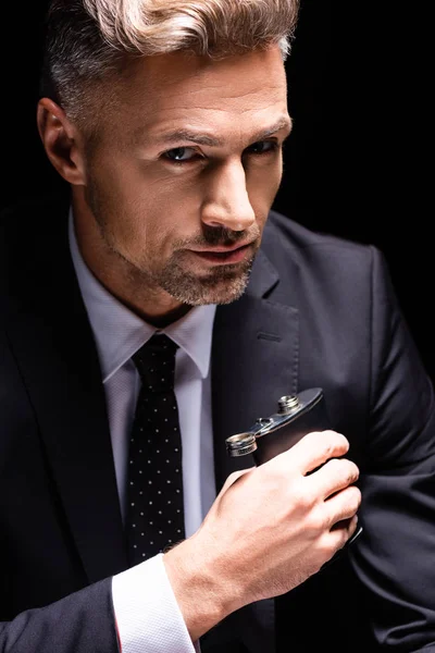 Confident businessman holding flask and looking at camera isolated on black — Stock Photo