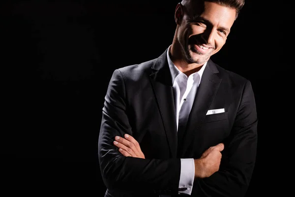 Smiling businessman with crossed arms looking at camera isolated on black — Stock Photo