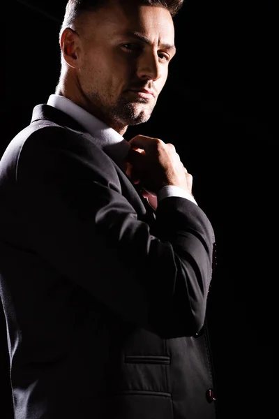 Handsome businessman adjusting shirt collar while looking at camera isolated on black — Stock Photo