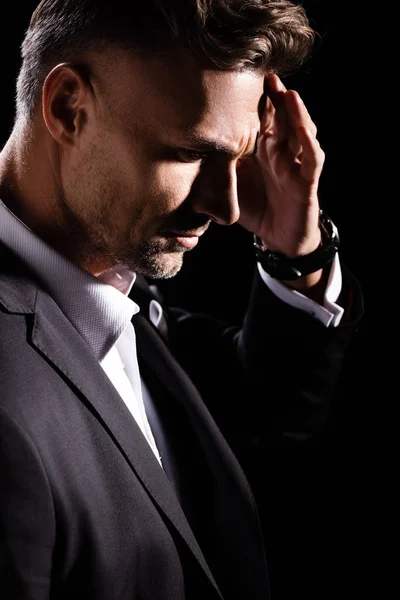 Vista lateral de empresario pensativo con la mano por la cabeza mirando hacia abajo aislado en negro - foto de stock