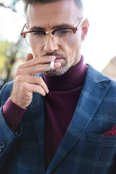 Bonito empresário fumando cigarro e olhando para baixo ao ar livre — Fotografia de Stock