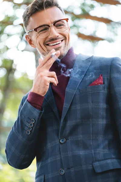 Guapo hombre de negocios fumando cigarrillo mientras sonríe al aire libre - foto de stock