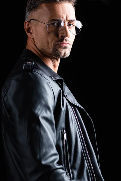 Side view of handsome man in leather jacket looking at camera isolated on black — Stock Photo