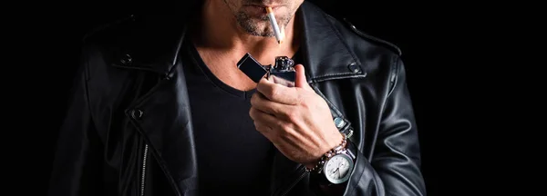 Vista cortada do homem em couro jaqueta de iluminação cigarro com isqueiro isolado em preto, tiro panorâmico — Fotografia de Stock