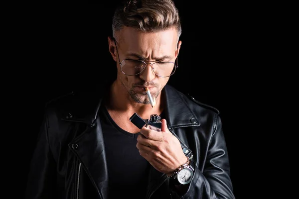 Bel homme en cuir veste éclairage cigarette avec briquet isolé sur noir — Photo de stock