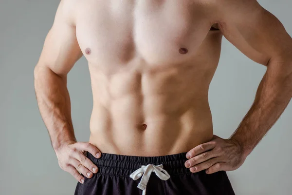 Ausgeschnittene Ansicht von sexy muskulösen Bodybuilder mit nacktem Oberkörper posiert mit Händen auf Hüften isoliert auf grau — Stockfoto