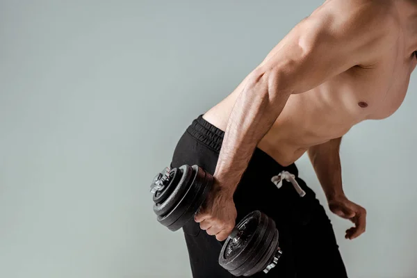 Vista parcial de culturista muscular sexy con torso desnudo ejercitando con mancuerna aislada en gris - foto de stock