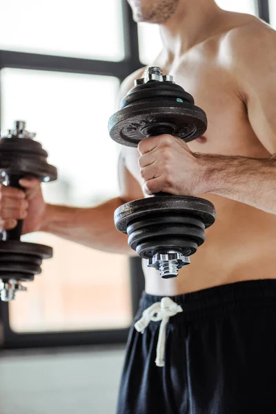 Partial view of sexy muscular bodybuilder with bare torso exercising with dumbbells — Stock Photo