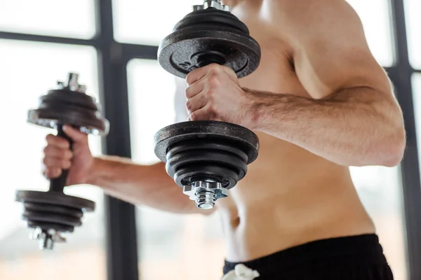 Partial view of sexy muscular bodybuilder with bare torso exercising with dumbbells — Stock Photo