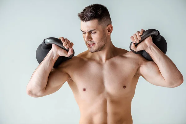 Sexy muscular bodybuilder with bare torso exercising with kettlebells isolated on grey — Stock Photo