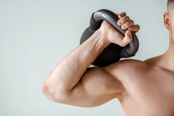 Partial view of sexy muscular bodybuilder exercising with kettlebell isolated on grey — Stock Photo