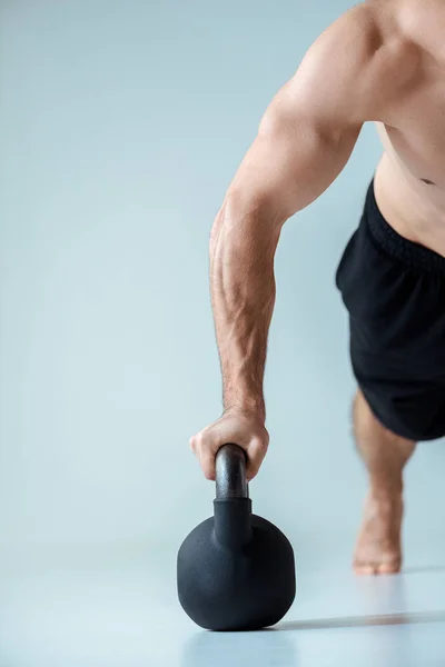 Partial view of sexy muscular bodybuilder with bare torso doing push ups with kettlebell isolated on grey — Stock Photo