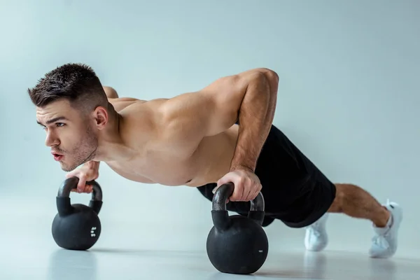 Sexy muskulöse Bodybuilderin mit nacktem Oberkörper macht Liegestütze mit Kettlebells auf grau — Stockfoto