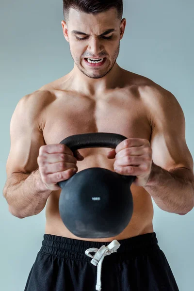 Tense sexy muscular bodybuilder with bare torso exercising with kettlebell isolated on grey — Stock Photo
