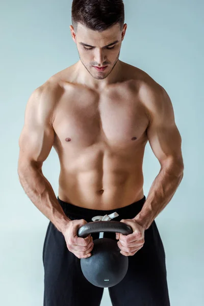 Sexy muscular bodybuilder with bare torso exercising with kettlebell isolated on grey — Stock Photo