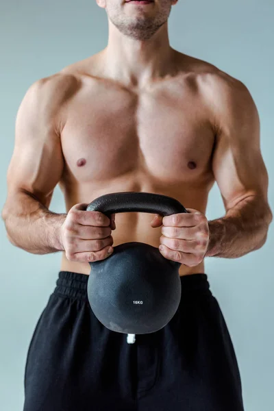 Partial view of sexy muscular bodybuilder with bare torso exercising with kettlebell isolated on grey — Stock Photo