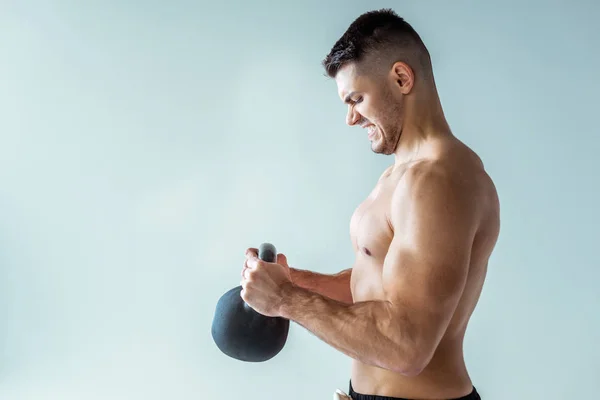 Seitenansicht des sexy muskulösen Bodybuilders mit nacktem Oberkörper beim Training mit der Kettlebell isoliert auf grau — Stockfoto