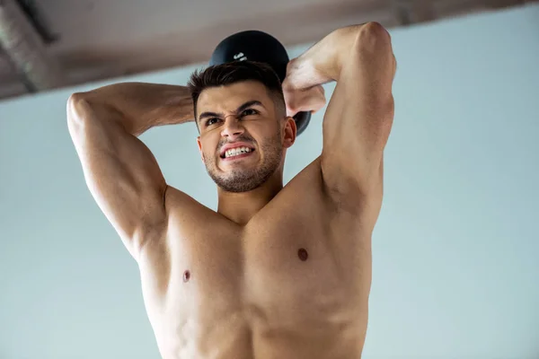 Low angle view of tense sexy muscular bodybuilder with bare torso exercising with kettlebell — Stock Photo