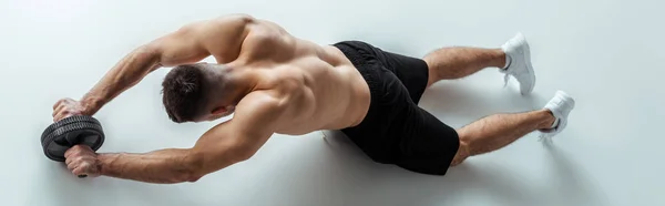 Overhead view of sexy muscular bodybuilder with bare torso exercising with ab wheel on grey background, panoramic shot — Stock Photo