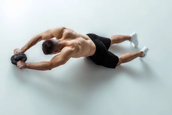 Вид зверху сексуальний м'язистий культурист з голим торсом вправи з коліщатком на сірому фоні — стокове фото